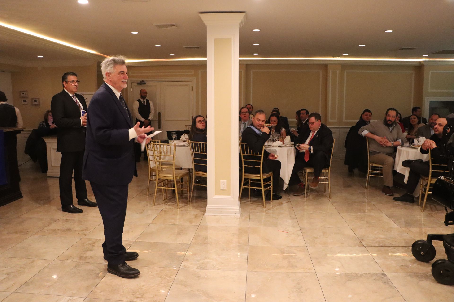 A Group Of People Seated At Tables Are Facing A Man In A Suit — Staten Island, NY — RCBA