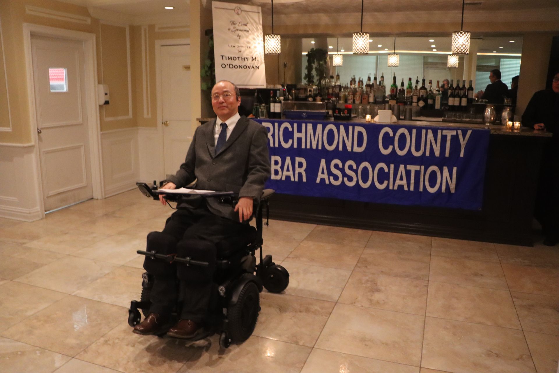 A Man In A Wheelchair Is Standing In Front Of A Richmond County Bar Association Sign — Staten Island, NY — RCBA