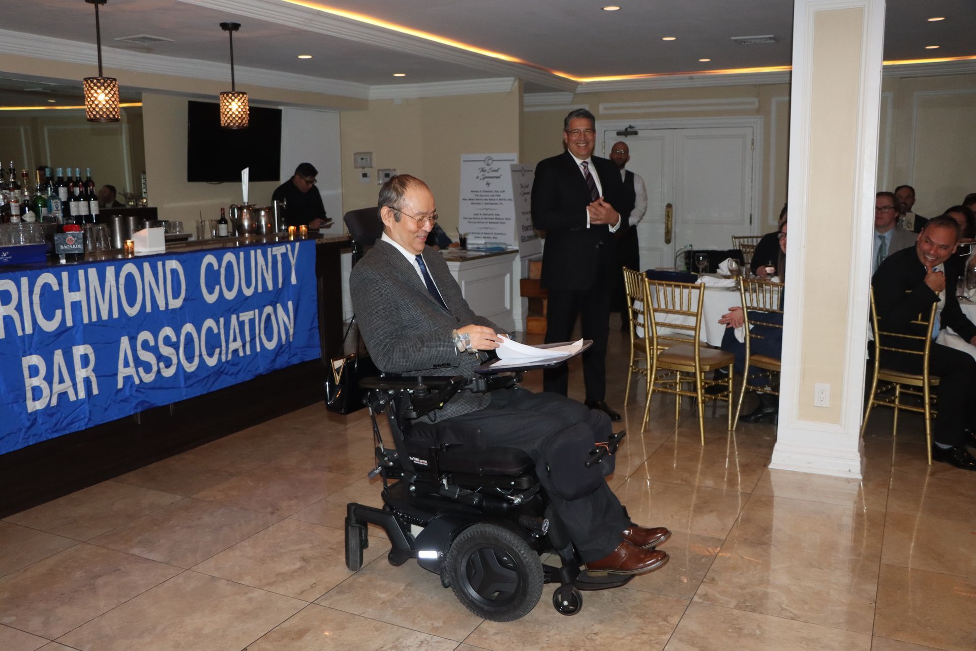 A Wheelchair-Using Man Is Seated In Front Of The Richmond County Bar Association Sign — Staten Island, NY — RCBA