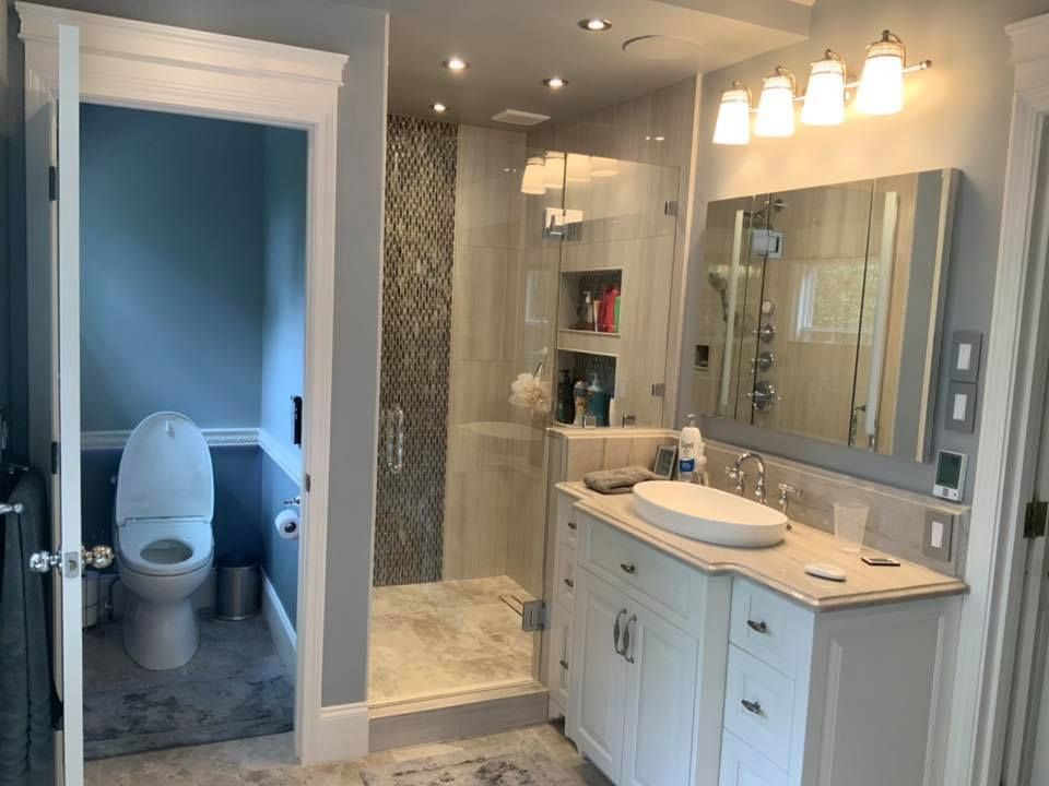 A bathroom with a toilet , sink , mirror and walk in shower.