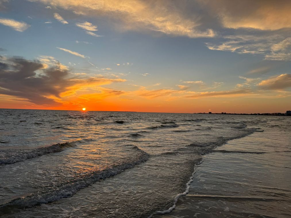 A vibrant sunset over the ocean, with orange and gold light reflecting on gentle waves washing onto a sandy beach.