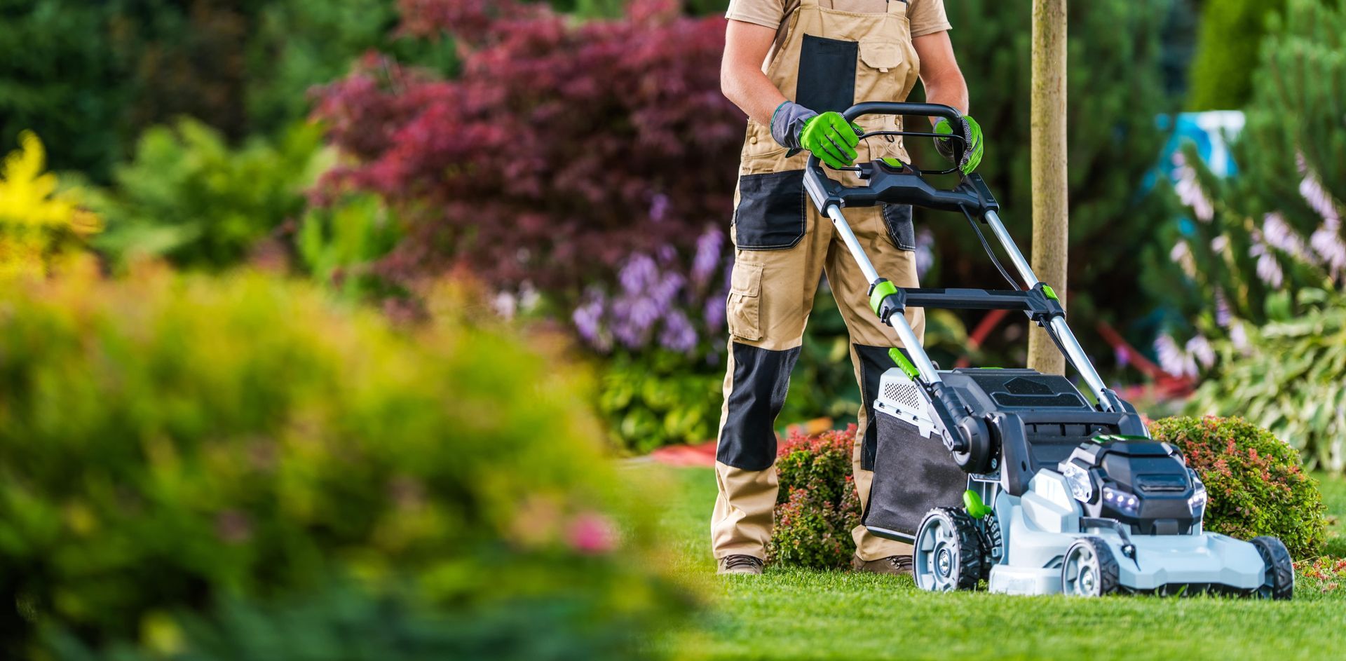 Person mowing a lawn with a green and silver lawn mower in a lush green garden.