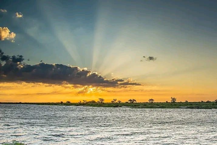 El sol brilla a través de las nubes sobre un cuerpo de agua.