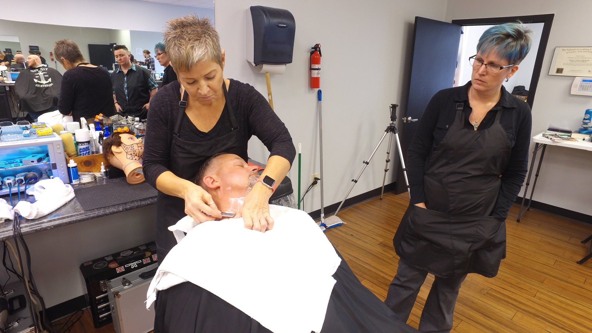 A woman is shaving a man 's beard in a barber shop.