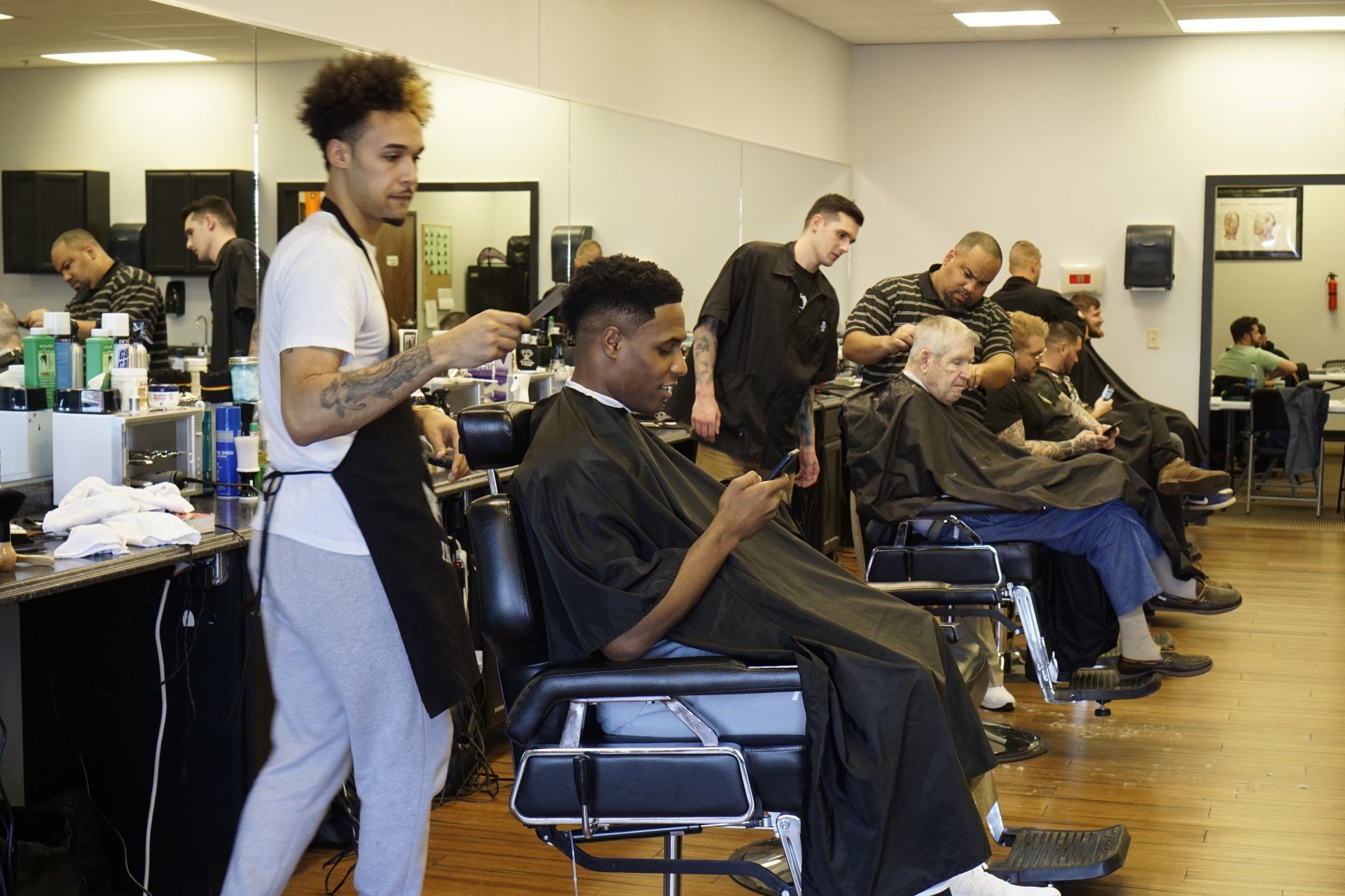A man is getting his hair cut at a barber shop while looking at his phone.