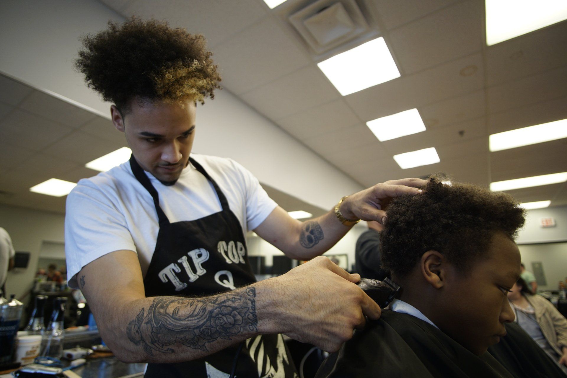 A man in an apron with the word tip on it is cutting a man 's hair