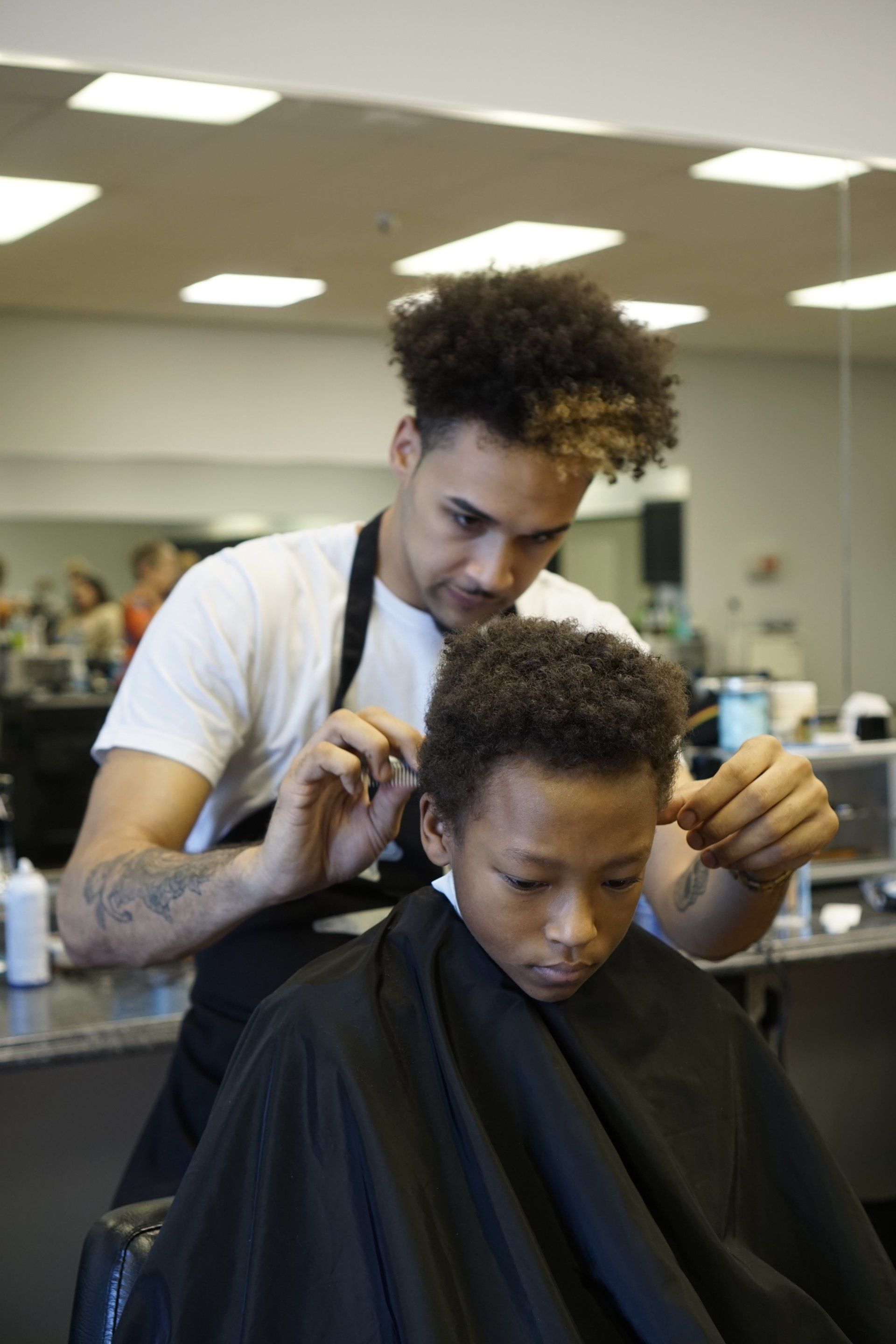 A young boy is getting his hair cut by a barber in a barber shop.