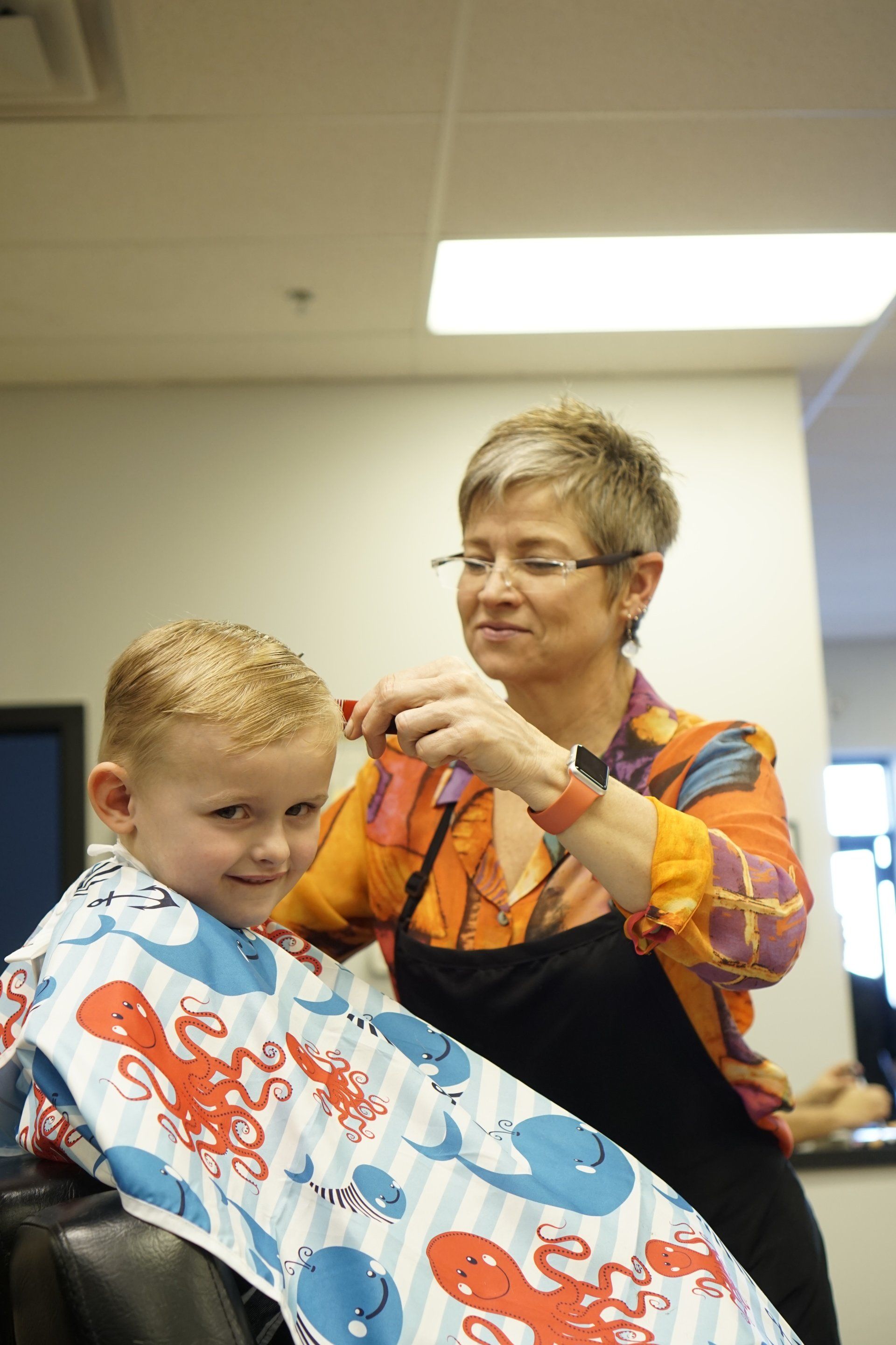 A woman is cutting a little boy 's hair in a barber shop.