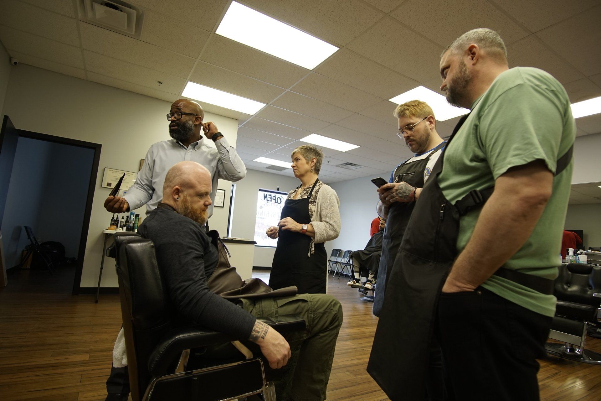 A group of people are standing around a man sitting in a barber chair.