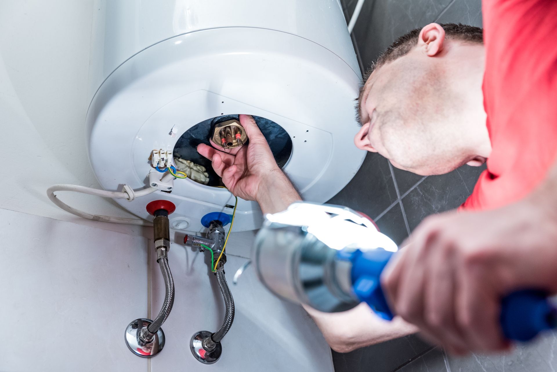 A plumber in the bathroom repairing an electric boiler.