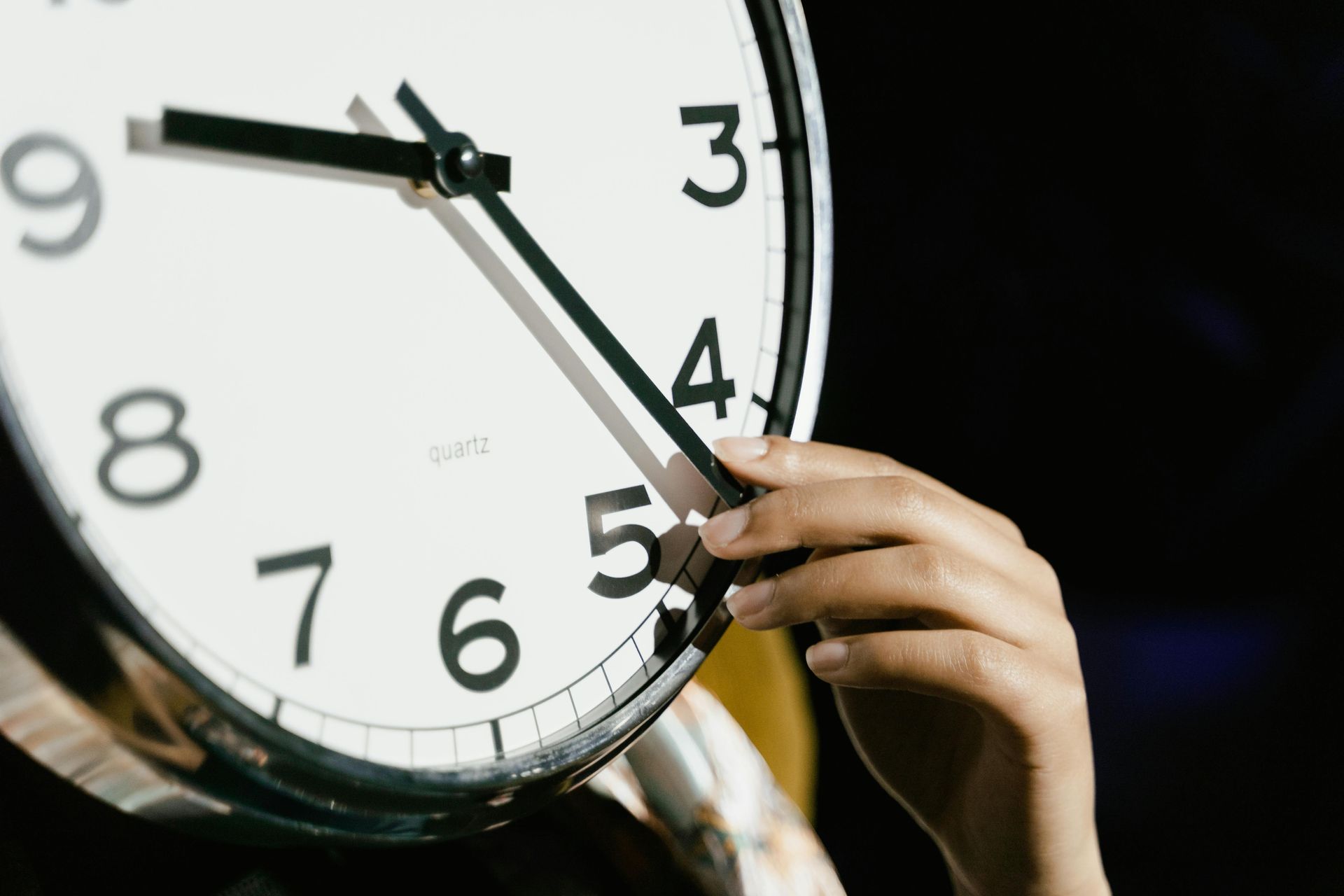 A hand adjusts the long hand of a wall clock, which is currently set to approximately 9:22.