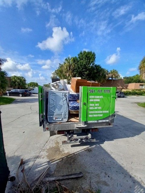 A green dumpster truck filled with junk is parked on the side of the road.