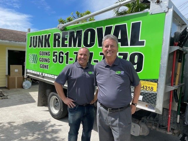 Two men are standing in front of a junk removal truck.