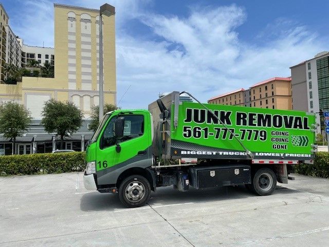 A row of green garbage trucks are parked under a bridge.