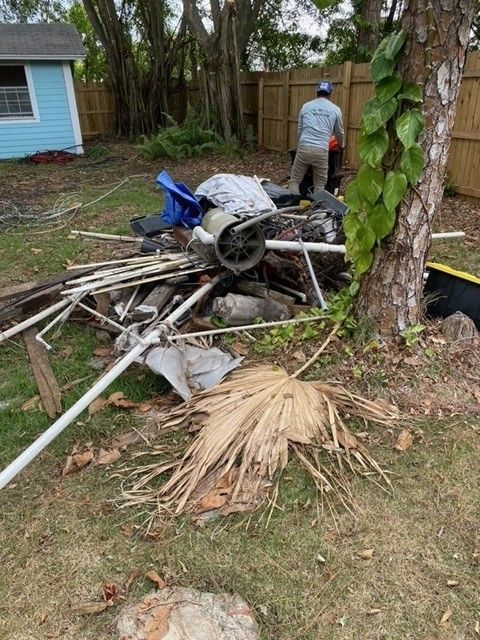 A man is standing next to a pile of trash in a backyard.