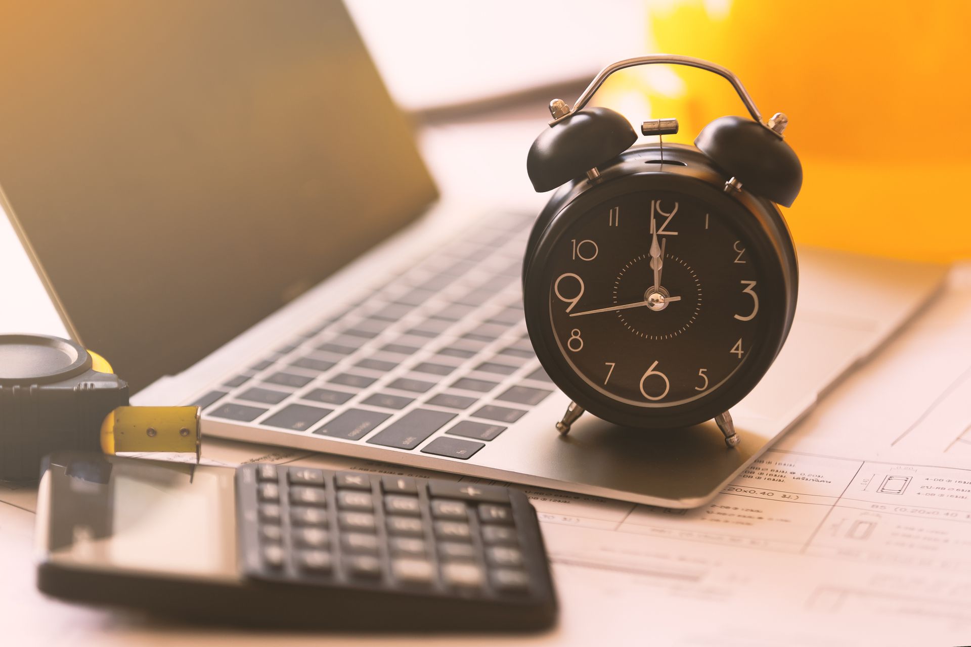An alarm clock is sitting on top of a laptop next to a calculator.