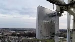 Cell tower antenna mounted on a metal structure, overlooking a town on an overcast day.