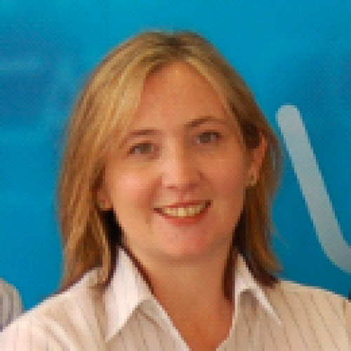 Woman with blonde hair smiling, wearing a white collared shirt, blue background.