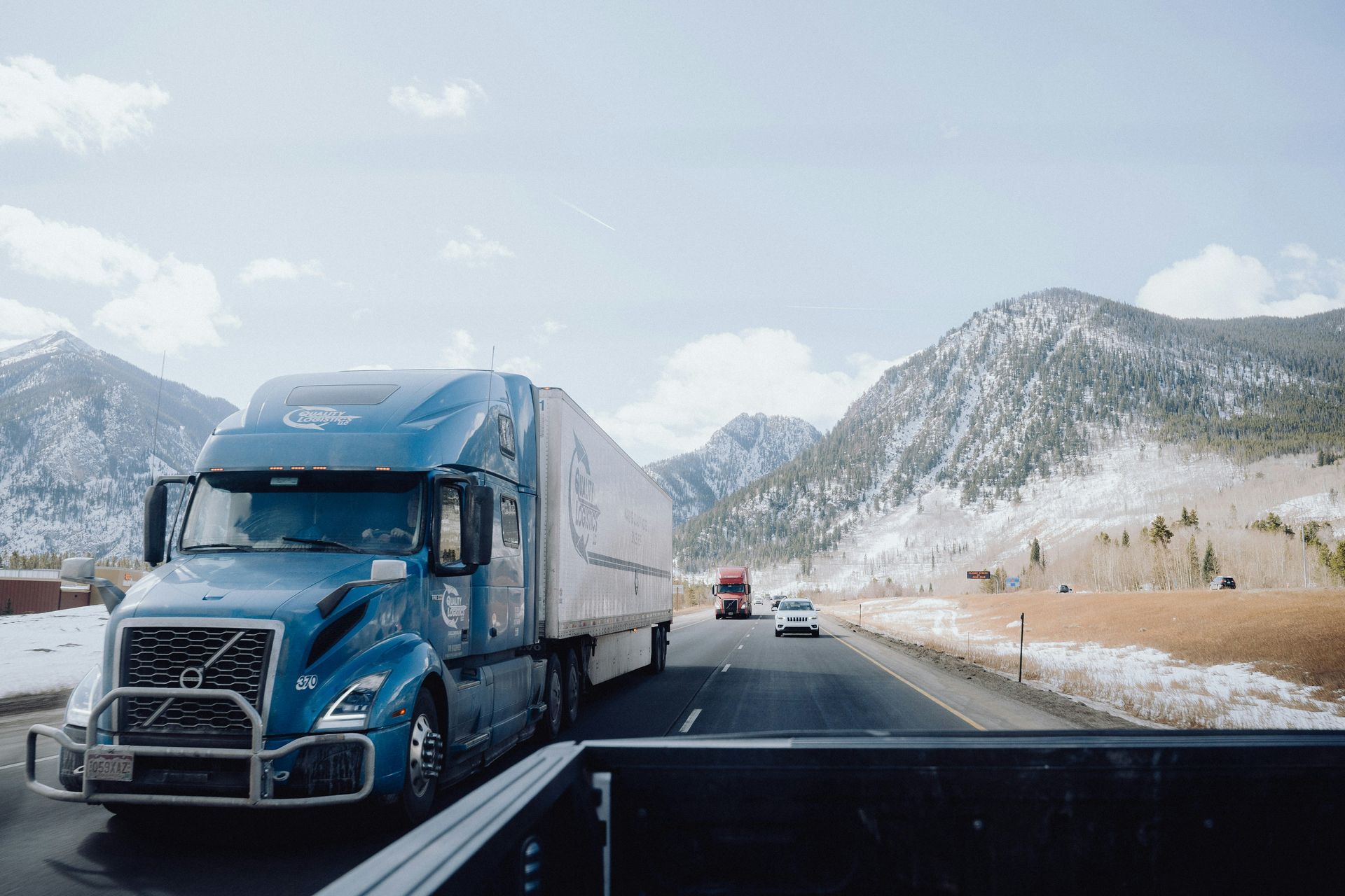 Blue semi-truck driving on a road with snowy mountains in the background. Sunny day.