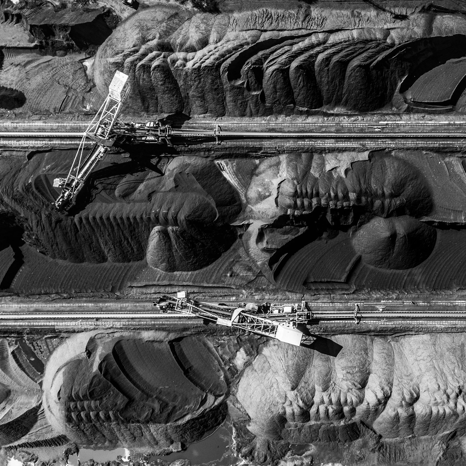 Overhead view of a coal mine with industrial machinery working on dark piles of material.