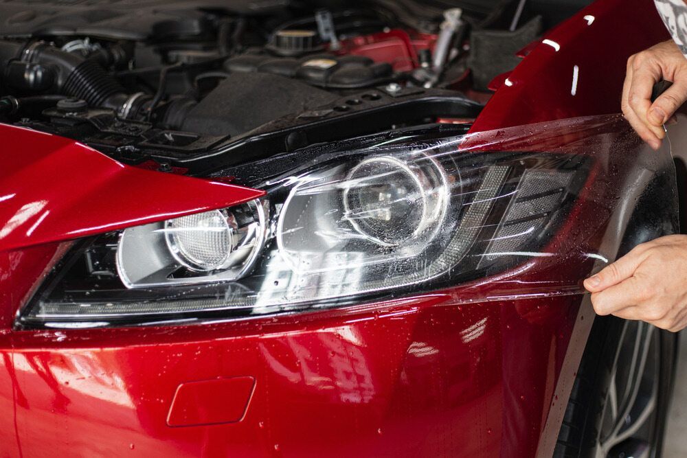 A Person is Applying a Protective Film to the Headlight of a Red Car — VIP Car Care Newcastle in Cardiff, NSW