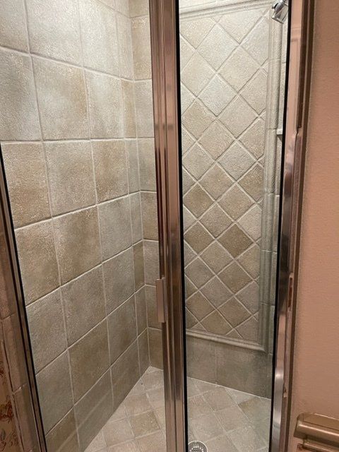 A walk in shower with a glass door and tiled walls.