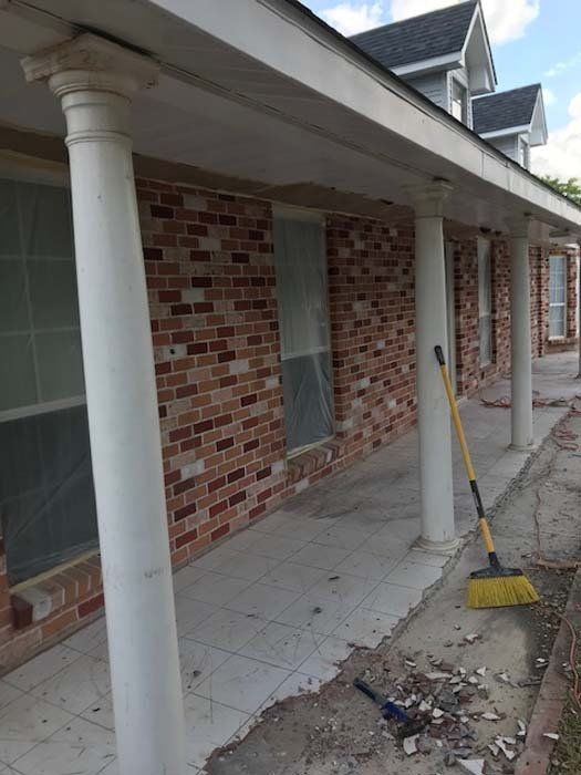 A brick house with columns and a broom on the sidewalk