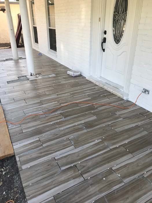 A porch with a wooden floor and a white house in the background.