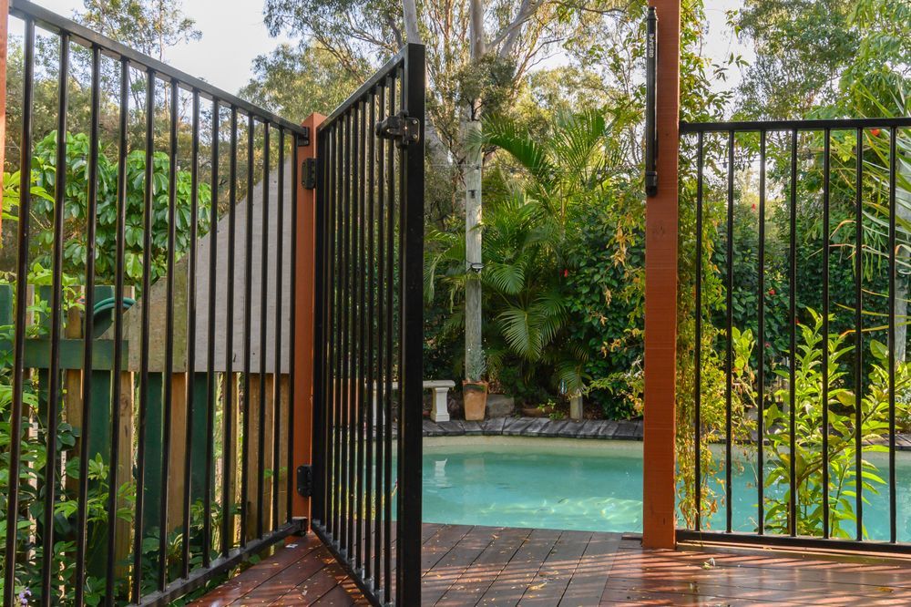A Black Metal Pool Fence and Open Gate on a Wooden Deck — Sun Cool Pools & Spas in Maryborough, QLD