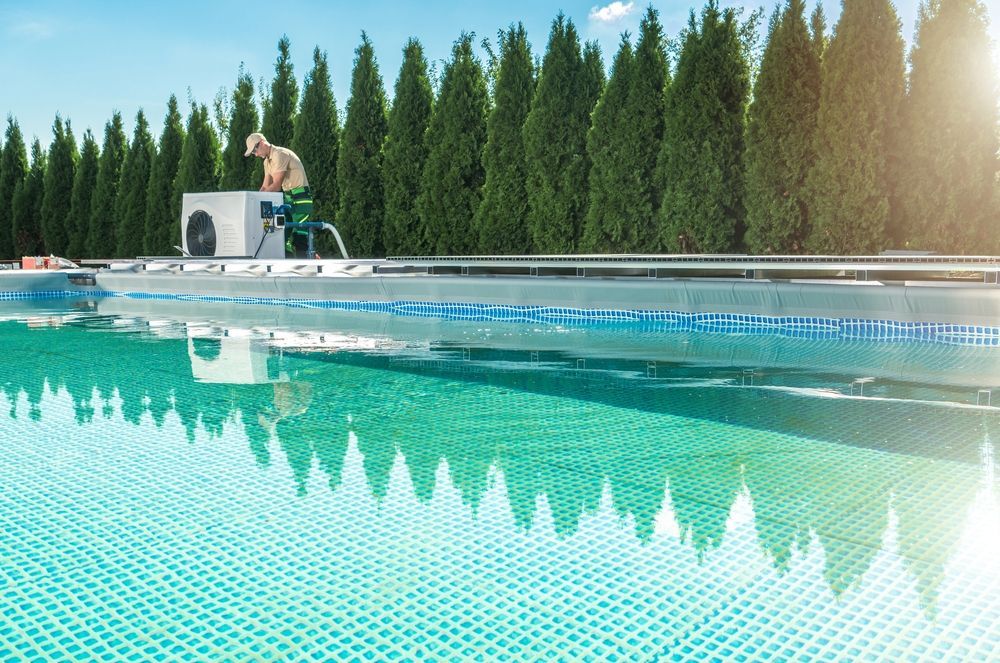 Person Working on a Pool With a Long Row of Evergreen Trees Behind It — Sun Cool Pools & Spas in Maryborough, QLD