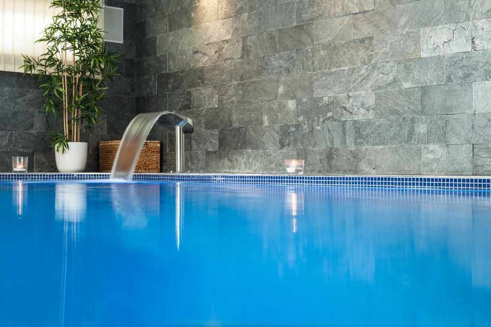 A Blue Indoor Swimming Pool With a Stone Wall Backdrop — Sun Cool Pools & Spas in Maryborough, QLD