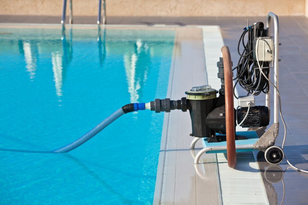 A Portable Pool Pump Sits on a Tiled Deck Next to a Clear Blue Pool — Sun Cool Pools & Spas in Maryborough, QLD
