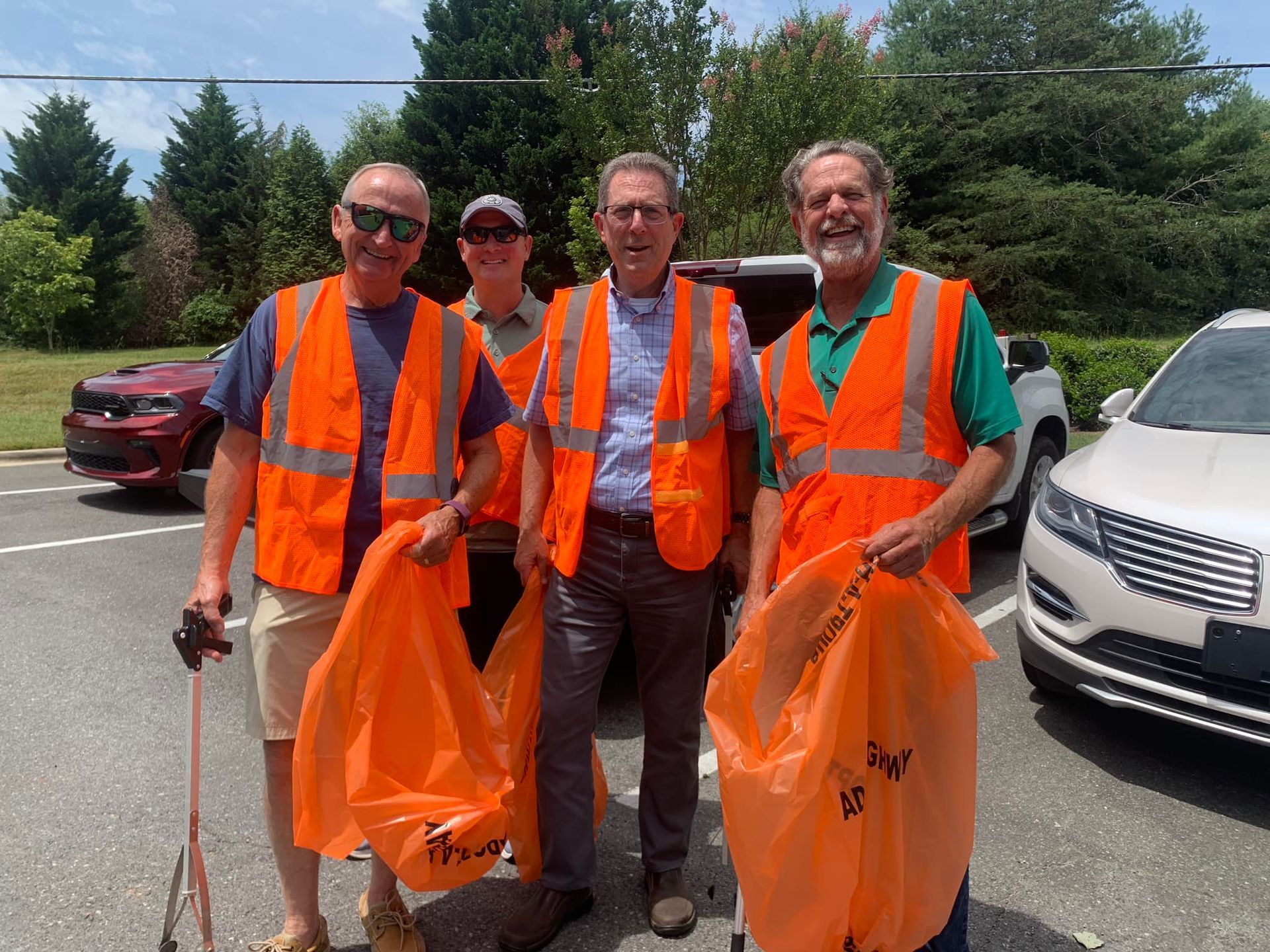 Rotary memebers wearing orange vests and safety vests and holding trash bags are preparing to pick up litter.