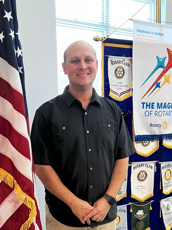 The Rotary Club emblem of a yellow gear with a white center on a white background.
