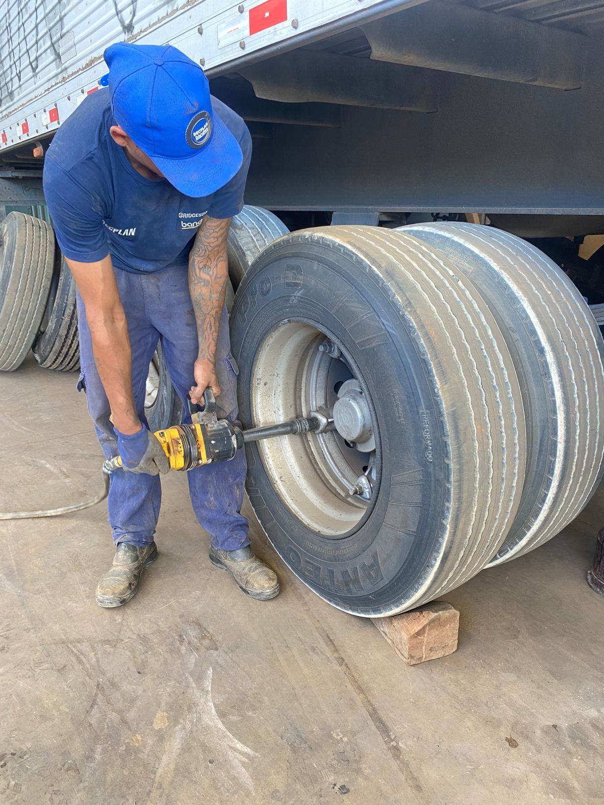 Pessoa utilizando uma ferramenta elétrica para remover um pneu de um caminhão; ao ar livre, durante o dia.