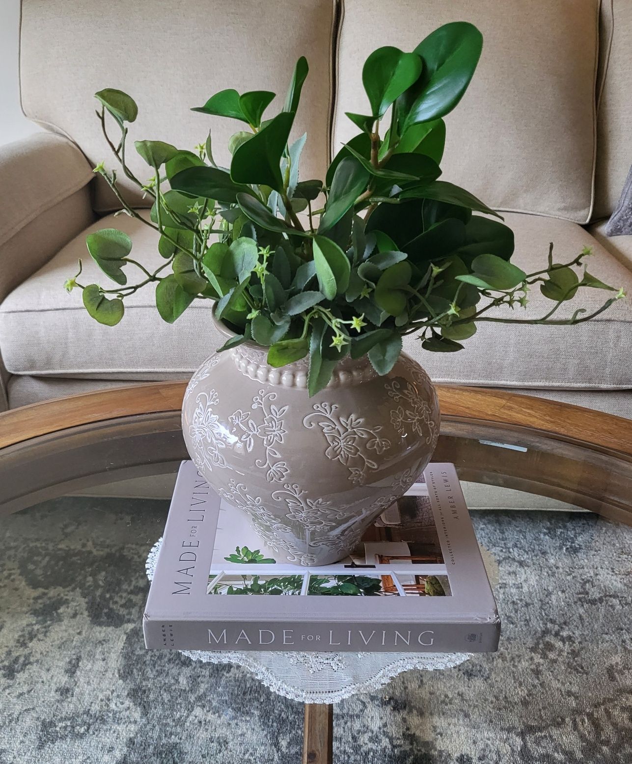 a vase of plants is sitting on top of a book on a coffee table .