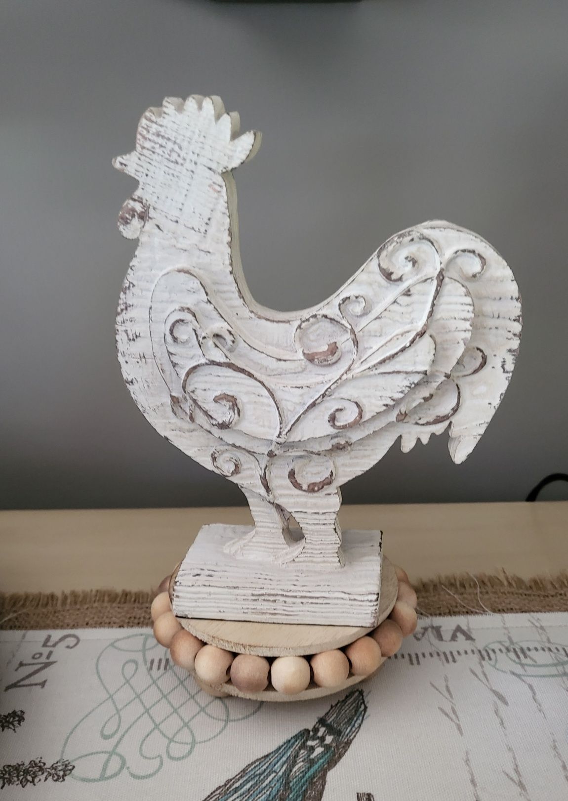 Interior decorating: a white wooden rooster is sitting on a table with wooden beads .
