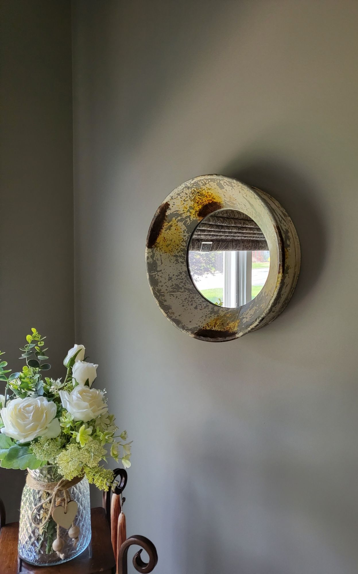 a round mirror is hanging on a wall next to a vase of flowers .