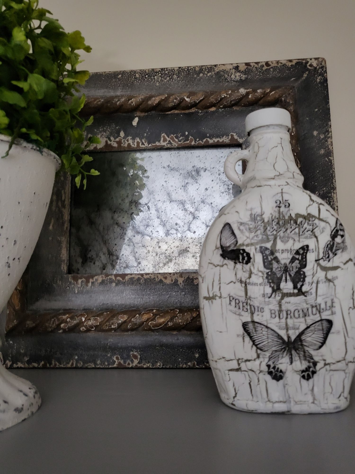 a bottle with butterflies on it is sitting on a table next to a picture frame with mirror