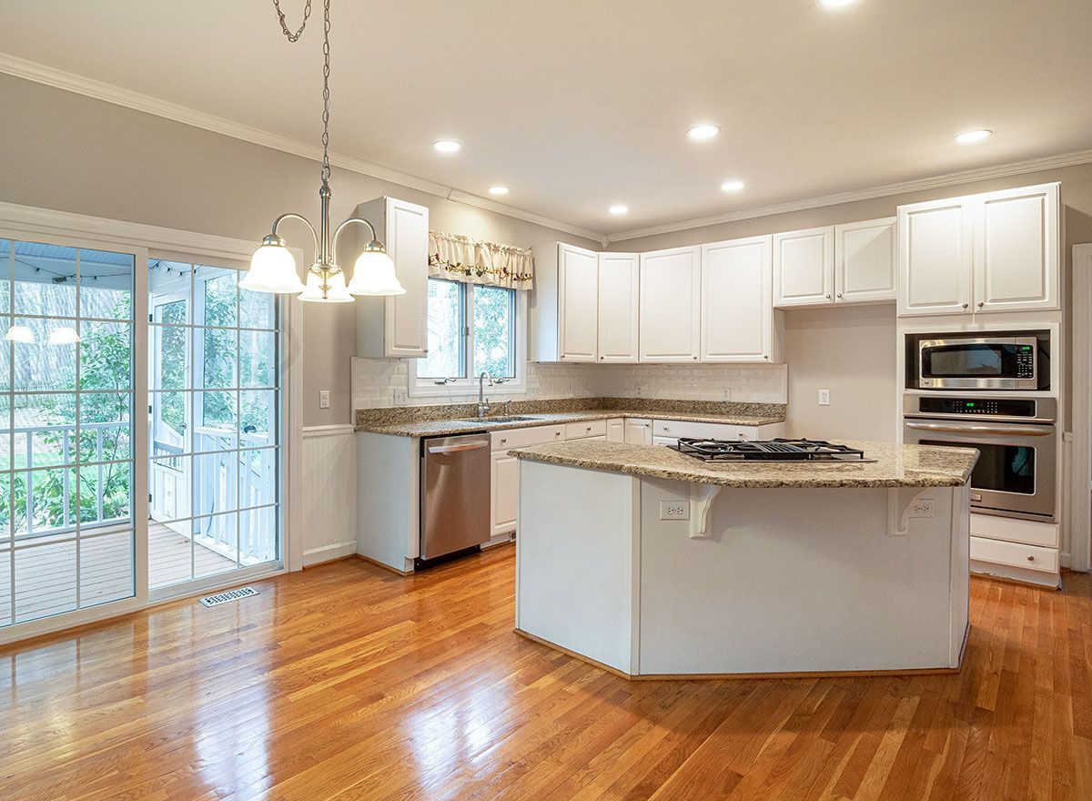 a kitchen with white cabinets , granite counter tops , stainless steel appliances and hardwood floors .
