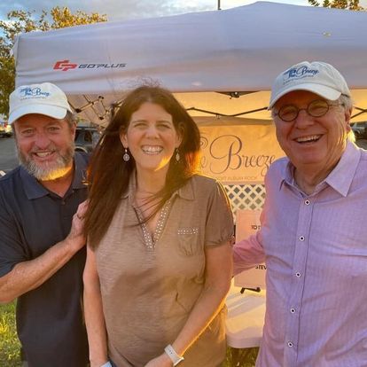Three people are posing for a picture in front of a tent that says breeze