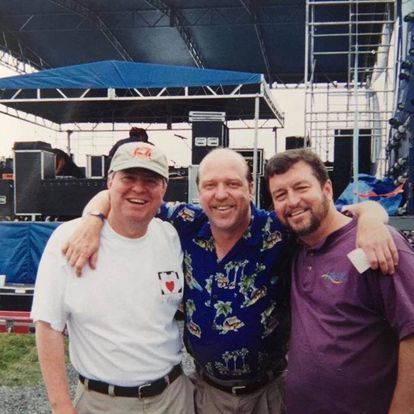 Three men posing for a picture with one wearing a hat with the letter a on it