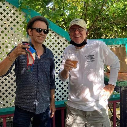 Two men are standing next to each other holding glasses of beer.