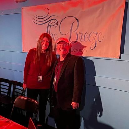 A man and a woman are standing in front of a sign that says the breeze