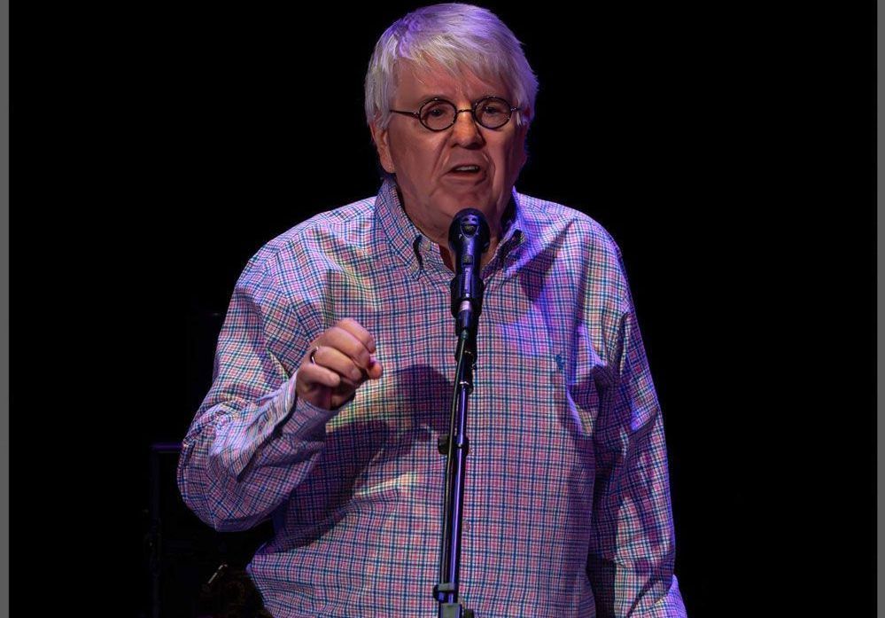 A man with glasses is singing into a microphone on a stage.