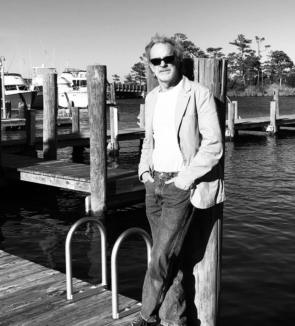 A man is standing on a dock next to a body of water.