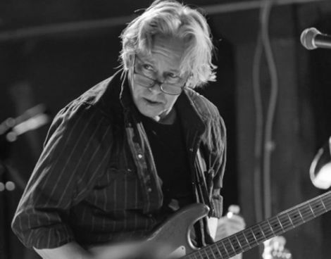 A man with glasses is playing a guitar in a black and white photo