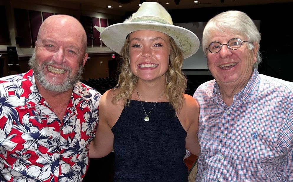 A woman in a hat is posing for a picture with two men.