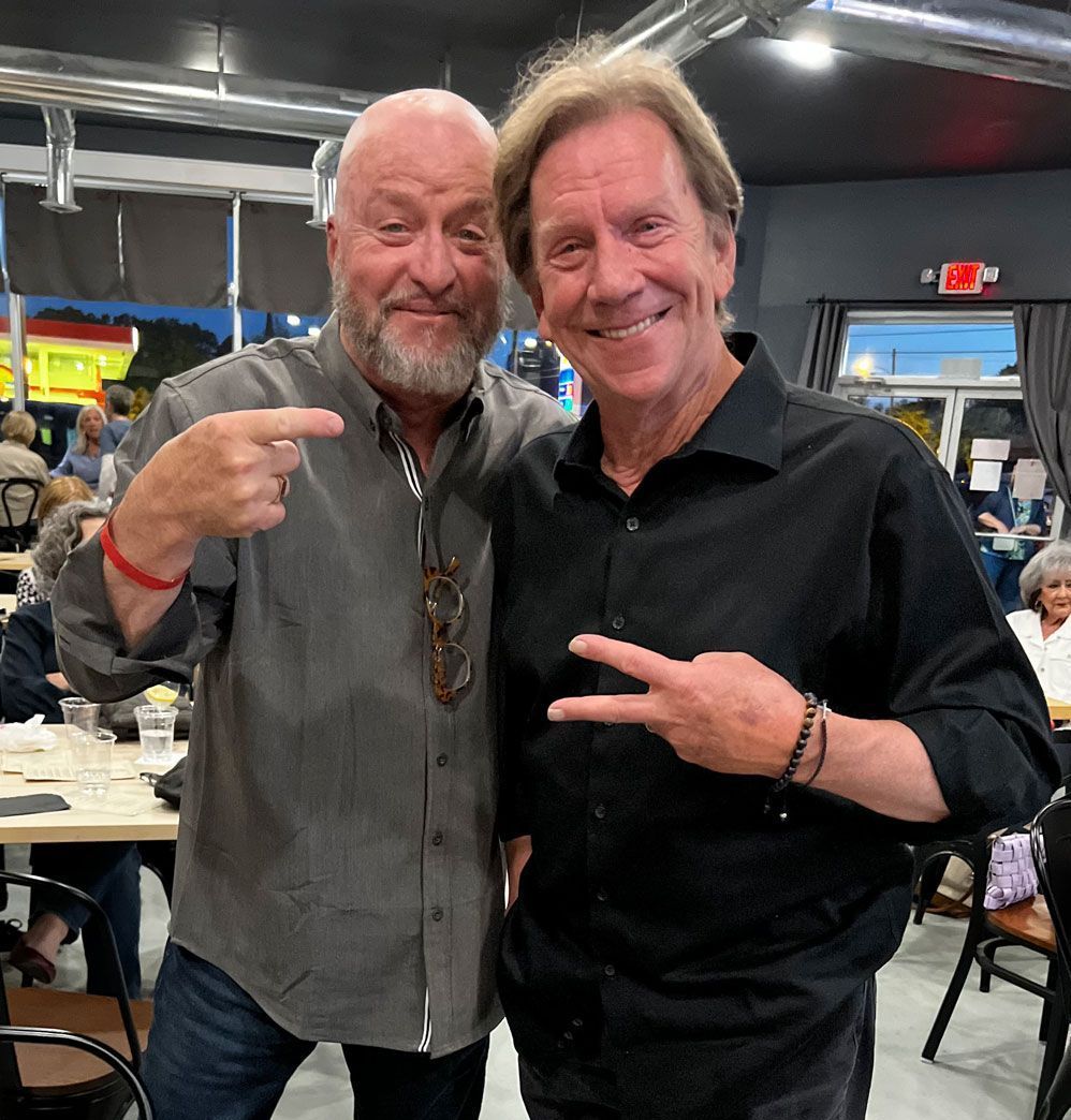 Two men are posing for a picture and one is pointing at the camera