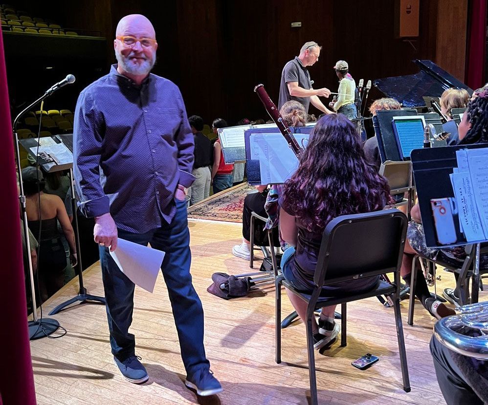 A man is standing on a stage in front of an orchestra.